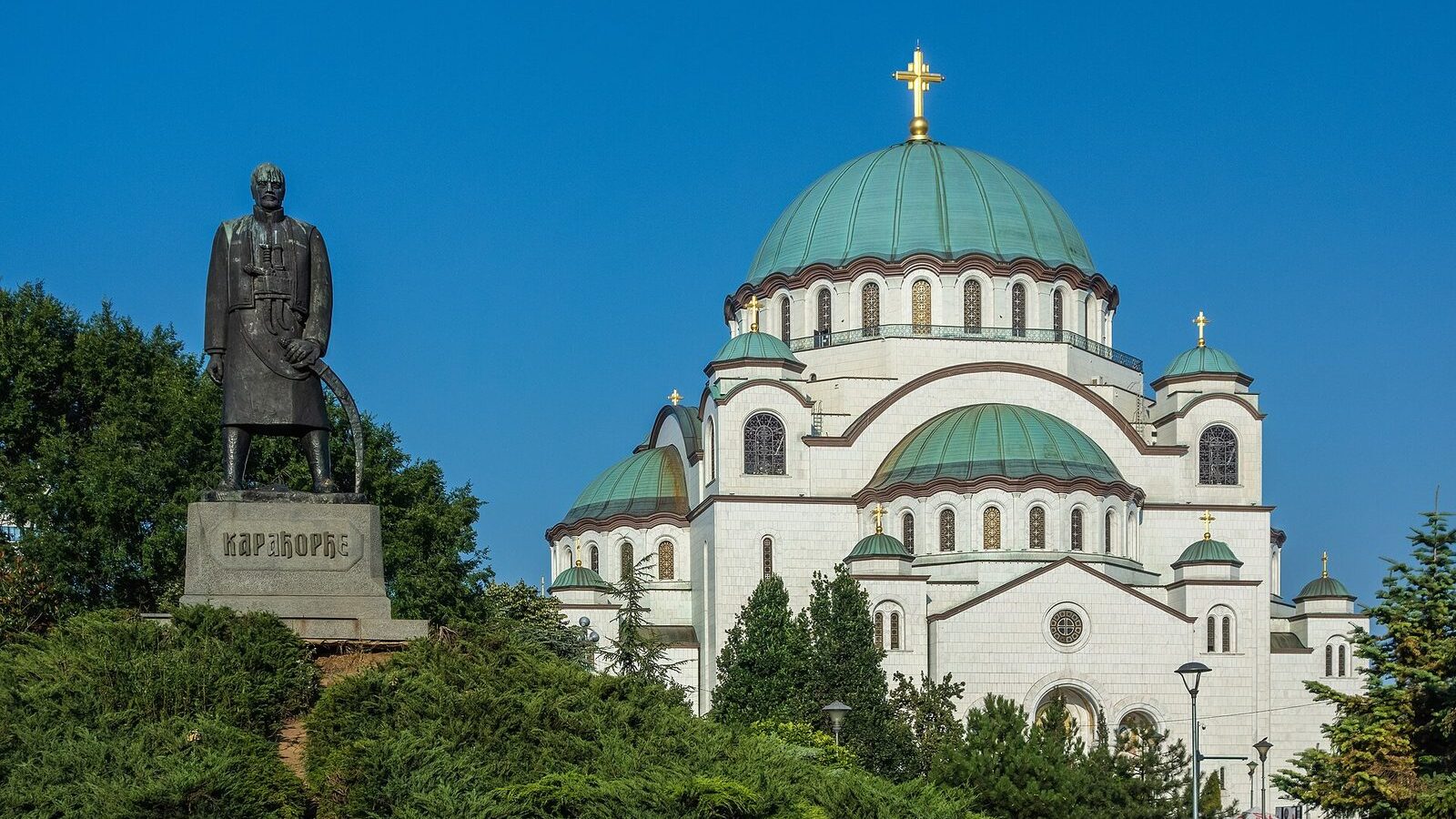 Храм Святого Саввы в Белграде: белый фасад с куполами на фоне неба и памятник Карагеоргию на переднем плане